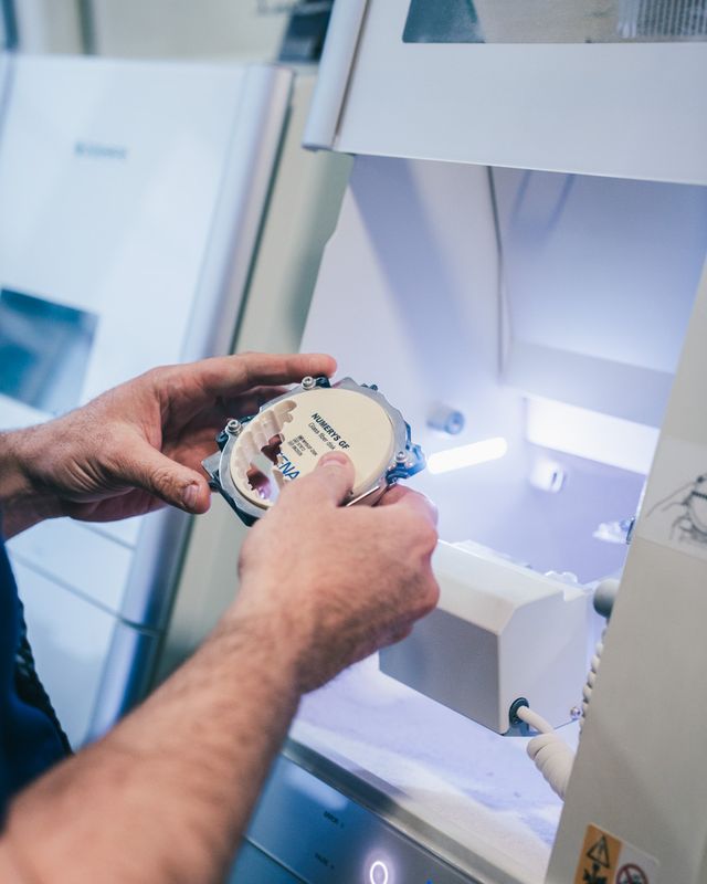 Prothésiste plaçant un disque de céramique dans l'usineuse pour fabriquer une prothèse